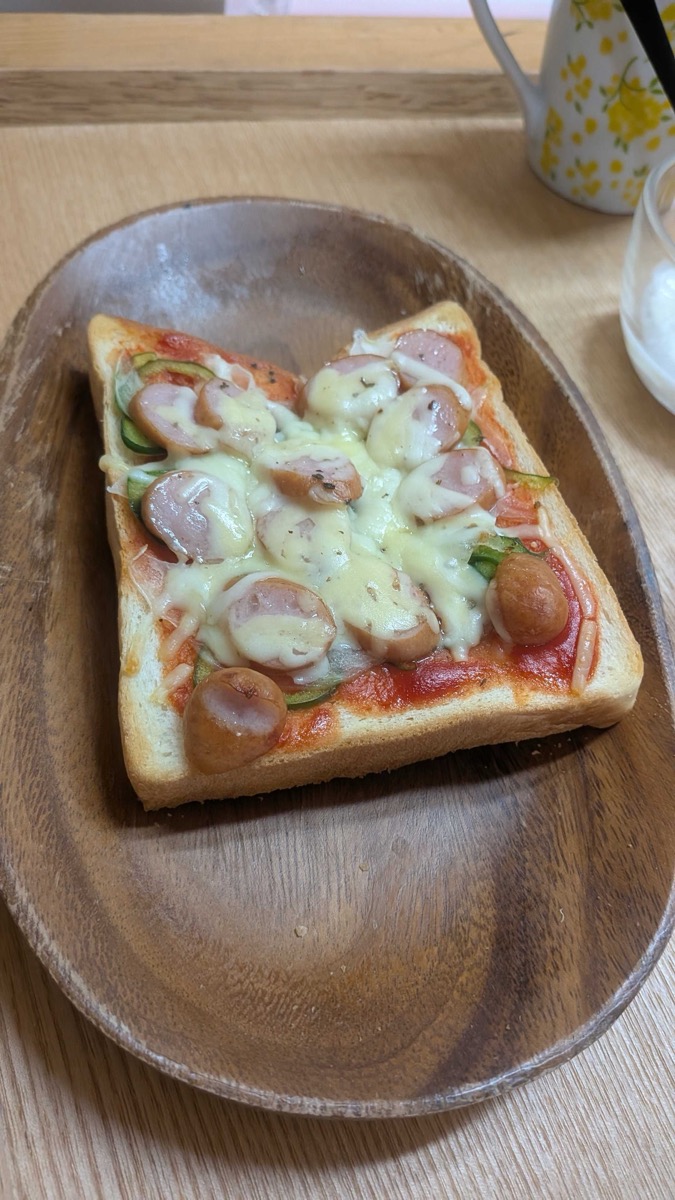 Pizza toast served on a wooden plate on a wooden table, with a mug in the background