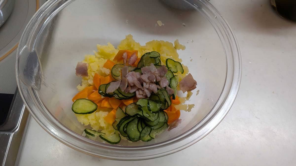 Mashed potato with carrot, cucumber, and ham added in a bowl before mixing