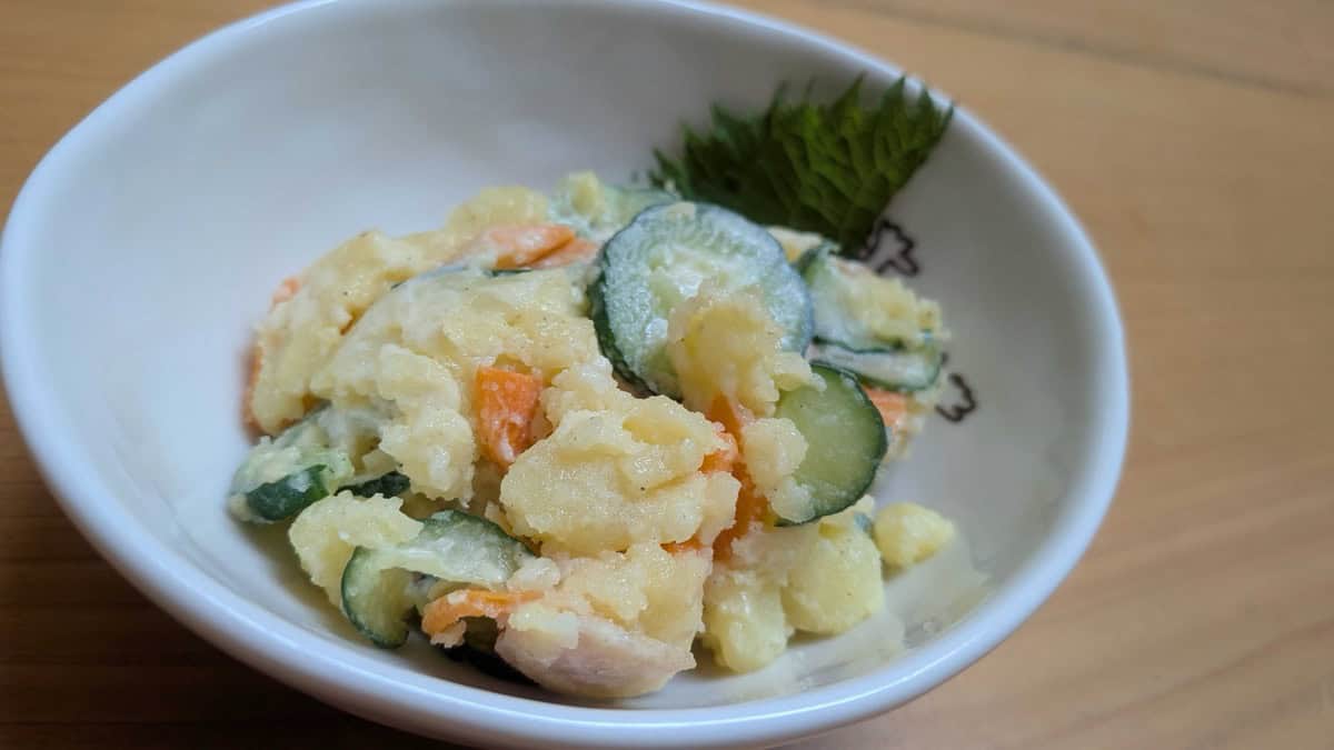 Japanese potato salad in a white bowl with a shiso leaf — creamy mashed potato with carrot, cucumber, and ham