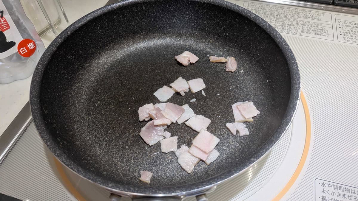 Pieces of bacon lightly frying in a pan