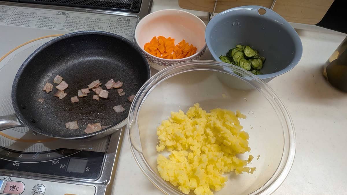 Prepped potato salad ingredients — mashed potato, fried bacon, sliced carrot, and cucumber