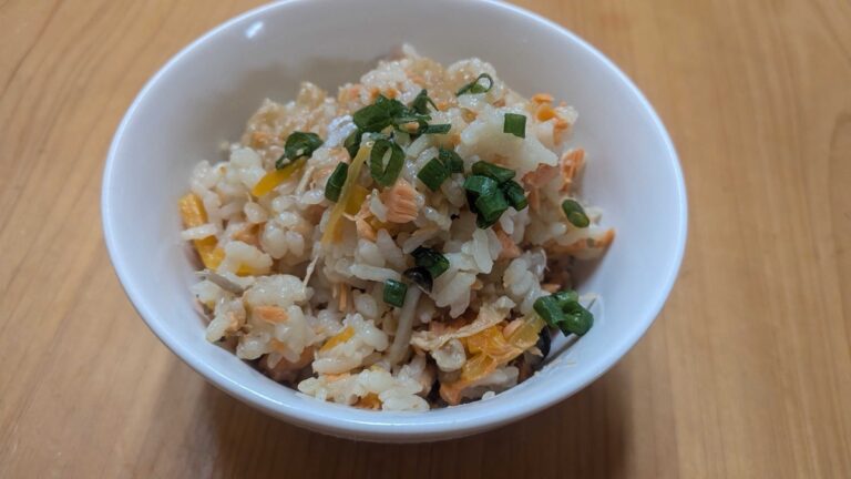 A bowl of salmon takikomi gohan — Japanese mixed rice with flaked salmon, mushrooms, carrot, and green onion
