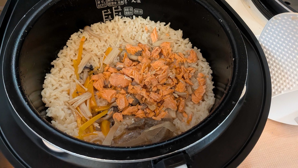 Flaked cooked salmon piled on top of the seasoned rice in the rice cooker