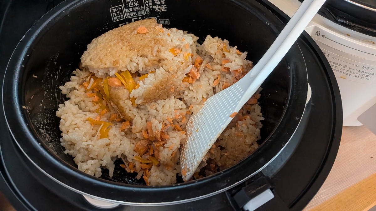 The salmon takikomi gohan being mixed together with a rice paddle in the pot