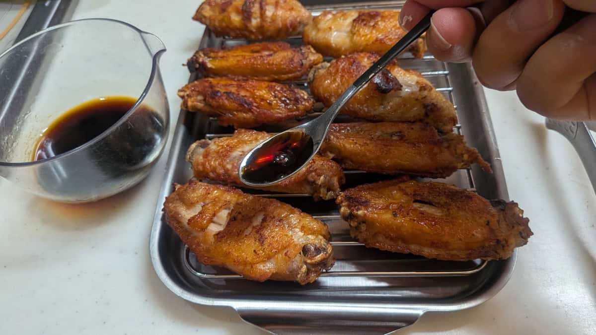 Brushing the sweet-savory sauce onto fried tebasaki wings with a spoon