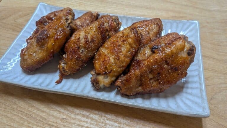 Nagoya-style tebasaki chicken wings on a white plate — deep-fried and glazed with sweet-savory sauce and pepper