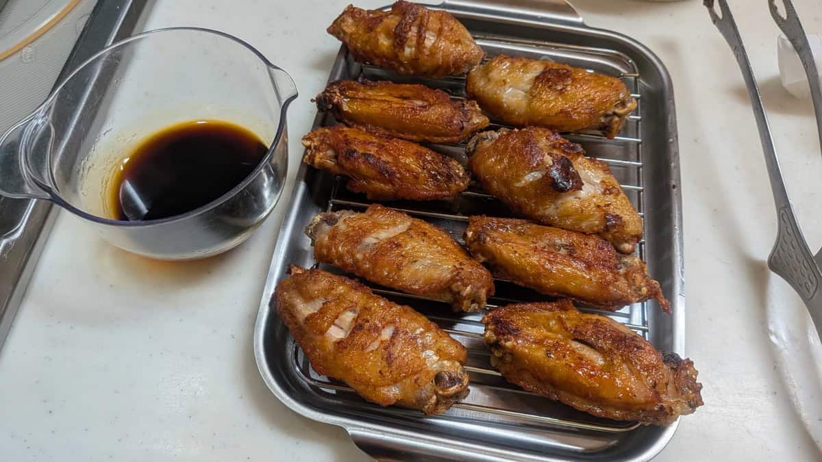 Deep-fried tebasaki wings on a rack next to a jug of sweet-savory sauce