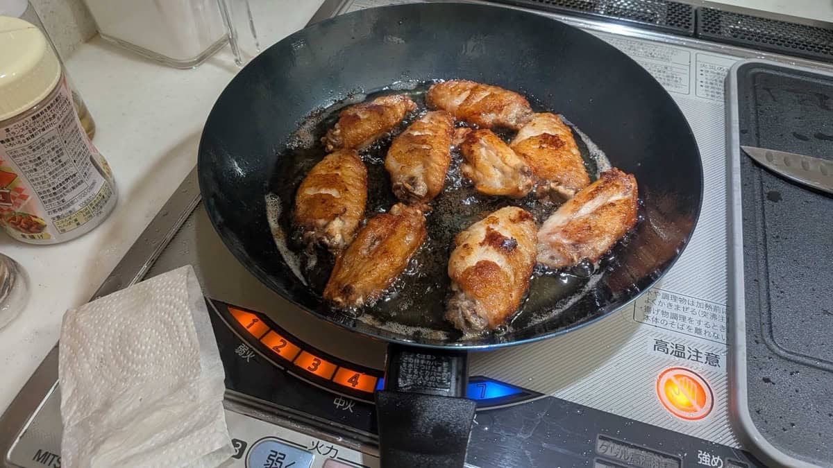 Chicken wings shallow-frying in oil in a frying pan on an induction cooktop