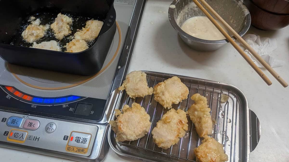 Tori ten frying in a pan on an induction cooktop with fried pieces draining on a wire rack