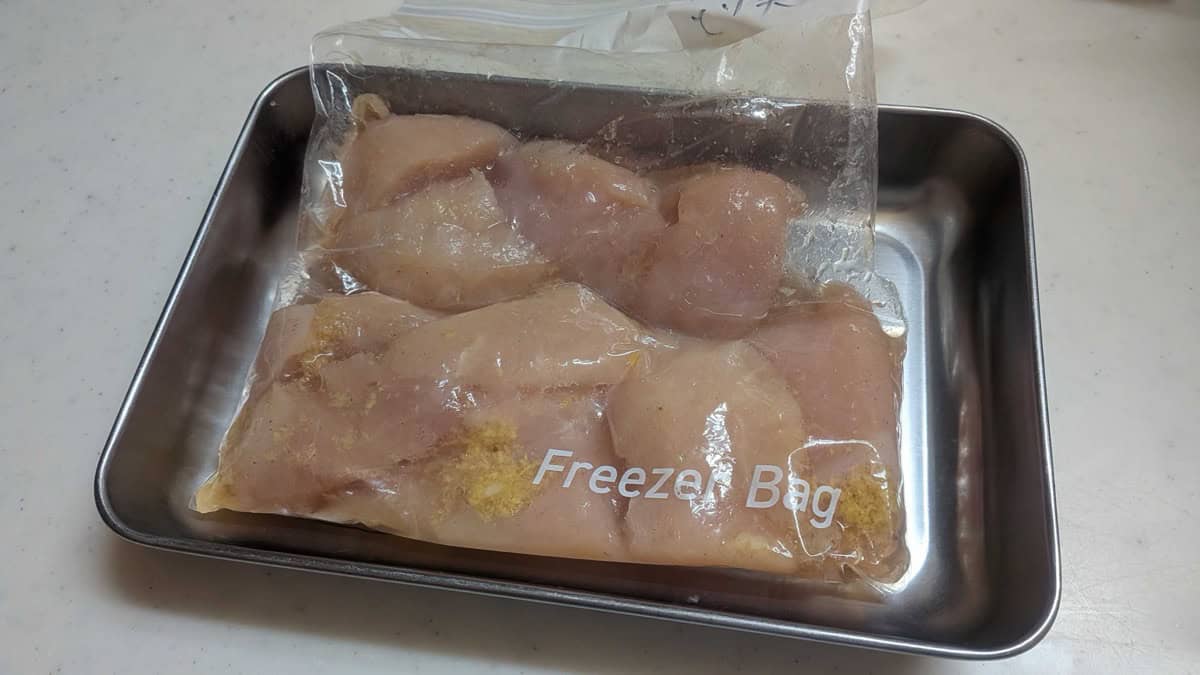 Chicken breast pieces marinating in soy sauce, sake, ginger, and garlic in a freezer bag