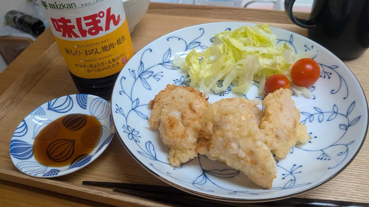 Tori ten served on a blue-and-white plate with shredded cabbage, cherry tomatoes, and a dish of ponzu
