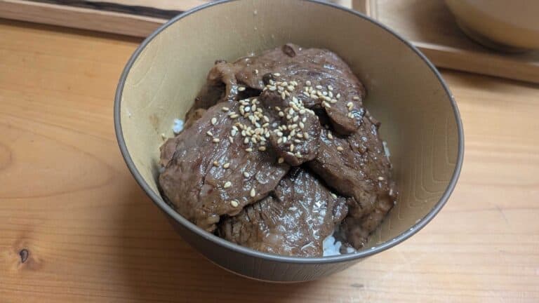 Yakiniku don — Japanese BBQ beef over rice in a wooden bowl, topped with toasted sesame seeds