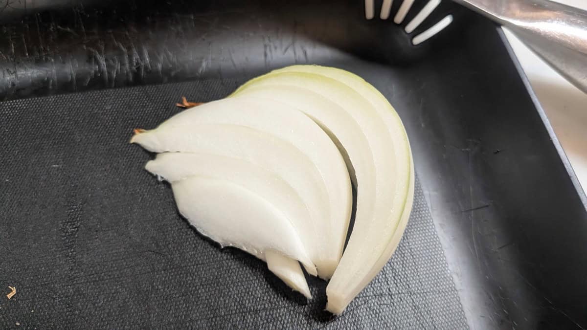Onion wedges on a black cutting board, ready to be grated for the marinade