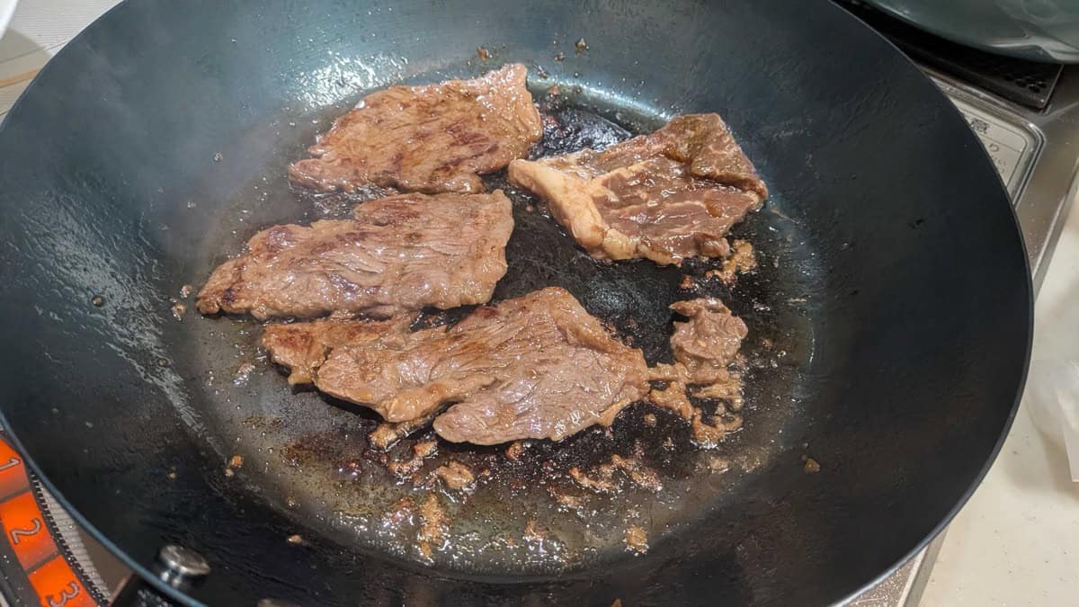 Marinated beef slices searing in a hot pan, browned at the edges