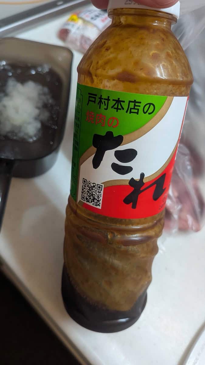 A bottle of Tomura Honten yakiniku sauce, a Miyazaki brand, held above the kitchen counter