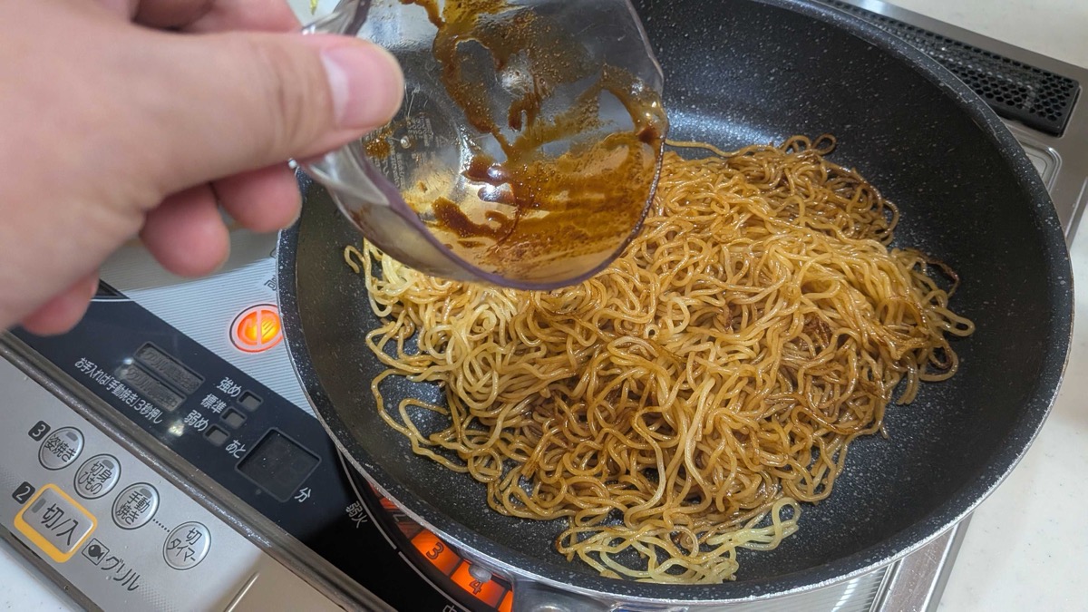 The dissolved yakisoba sauce being poured over the fried noodles in the pan