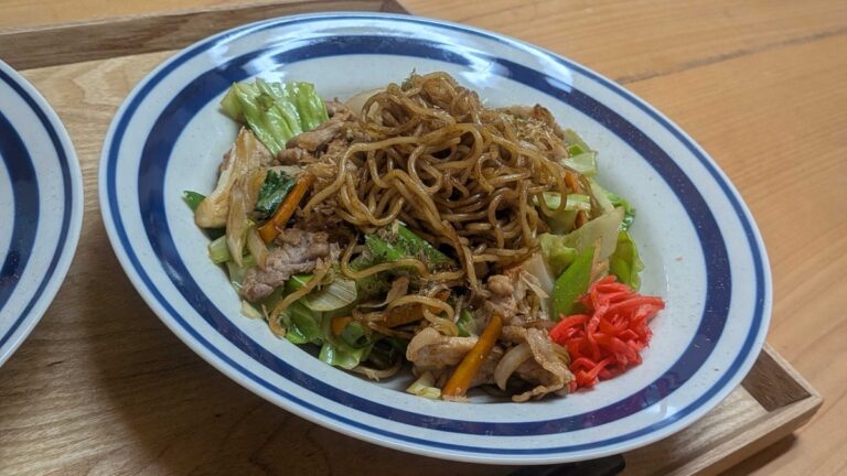 A plate of yakisoba — Japanese stir-fried noodles with pork, cabbage, carrot, bonito flakes, and red pickled ginger