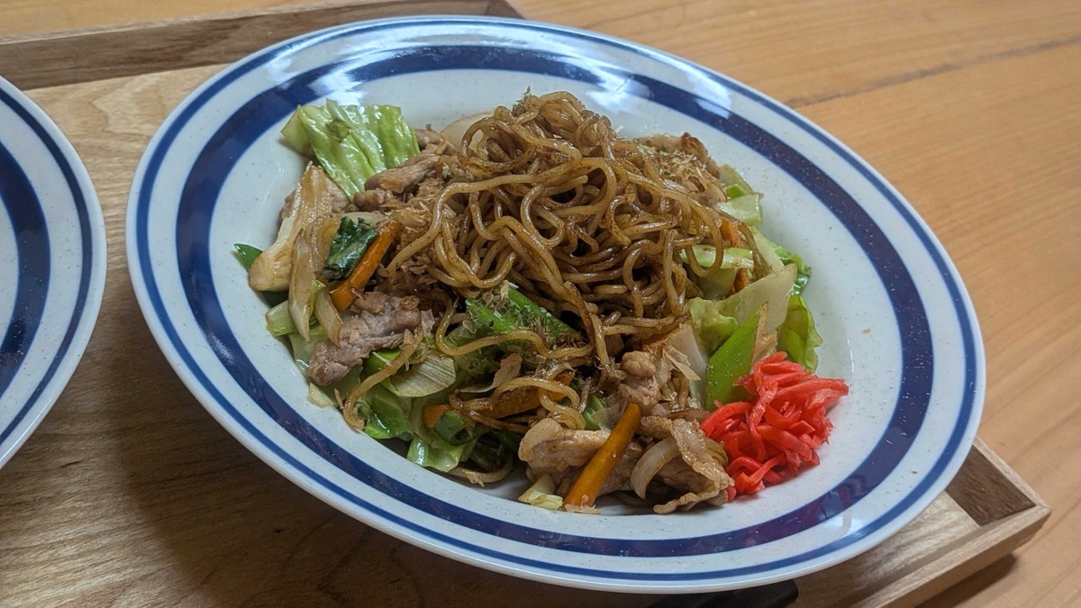 A plate of yakisoba — Japanese stir-fried noodles with pork, cabbage, carrot, bonito flakes, and red pickled ginger