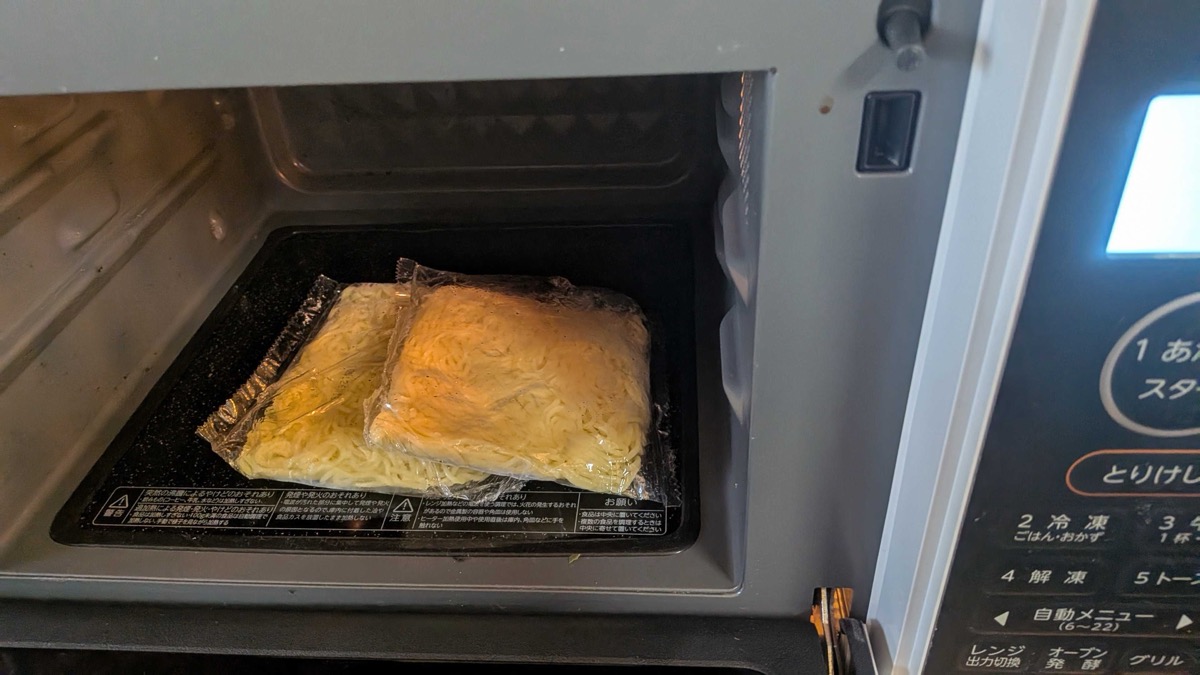 Yakisoba noodle bags, torn open slightly, warming in the microwave to loosen