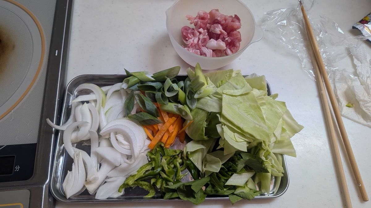 A tray of prepped vegetables — cabbage, onion, carrot, green pepper, green onion — with a bowl of sliced pork
