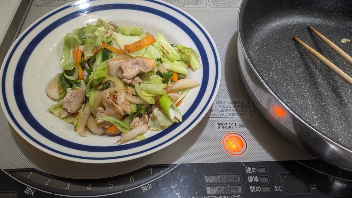Cooked pork and vegetables set aside on a plate next to the empty pan