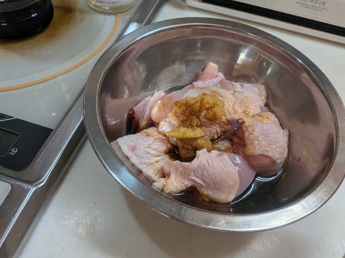 Soy sauce, sake, grated ginger, and grated garlic poured over cut chicken thigh in a mixing bowl