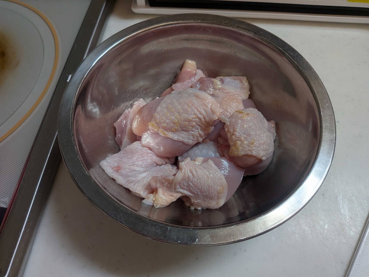 Raw chicken thigh cut into bite-sized pieces in a stainless steel mixing bowl