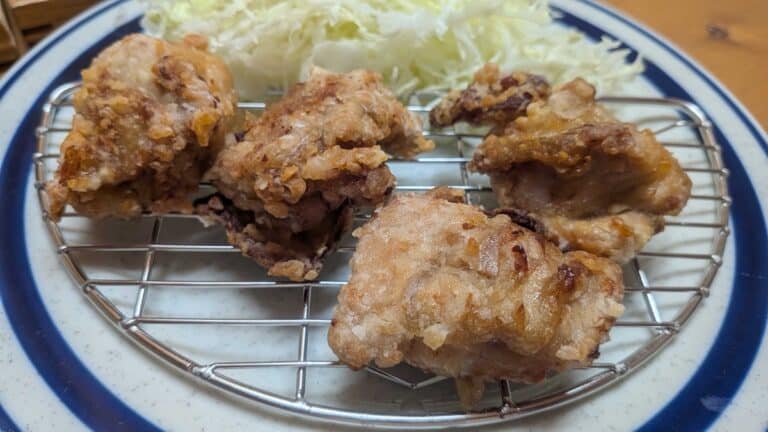 Air fryer karaage — golden Japanese fried chicken pieces on a wire rack over a blue-rimmed plate with shredded cabbage