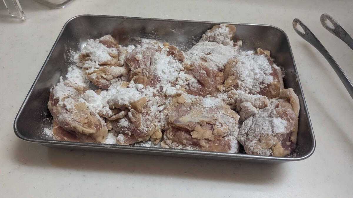 Marinated chicken pieces dusted with a first coat of white potato starch in a metal tray