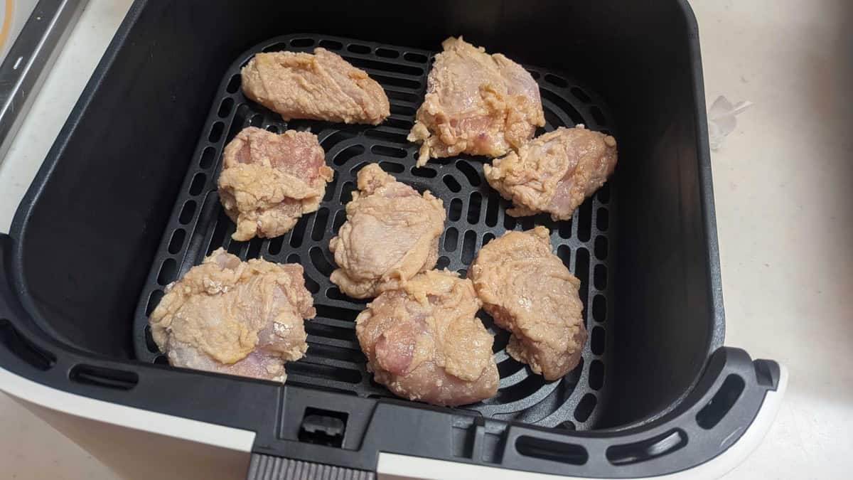 Eight pieces of coated raw karaage chicken arranged in a single layer in an air fryer basket