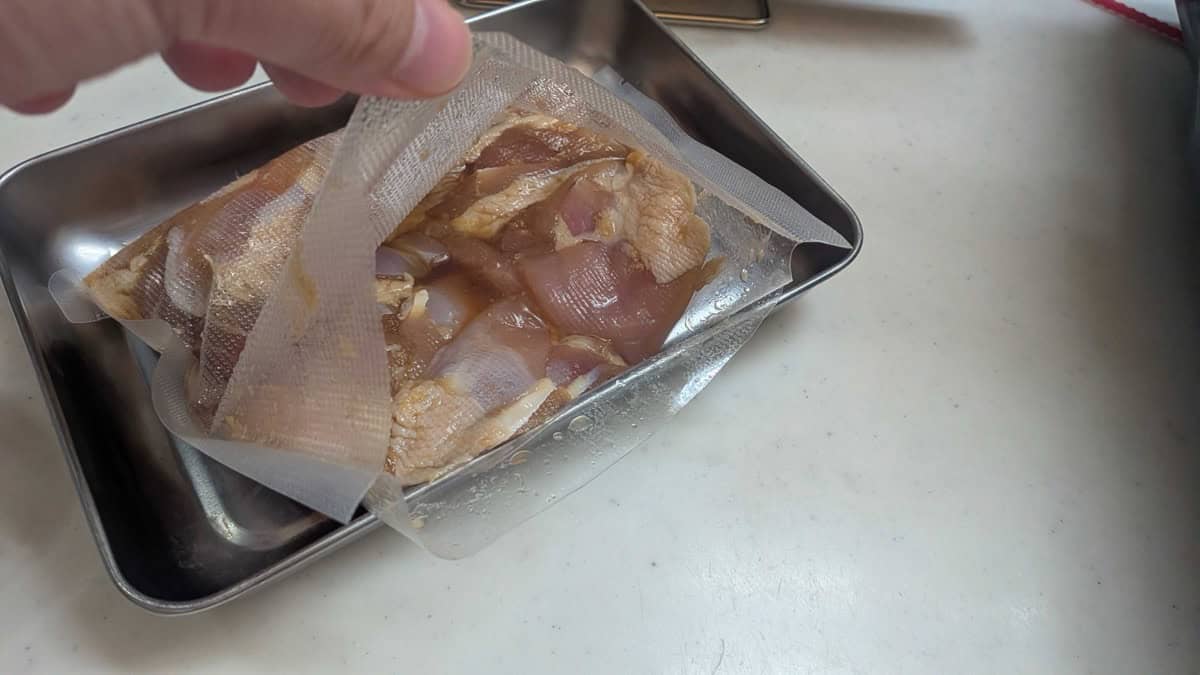 Chicken thigh pieces marinating in soy sauce, ginger, and garlic in a sealed bag in a metal tray