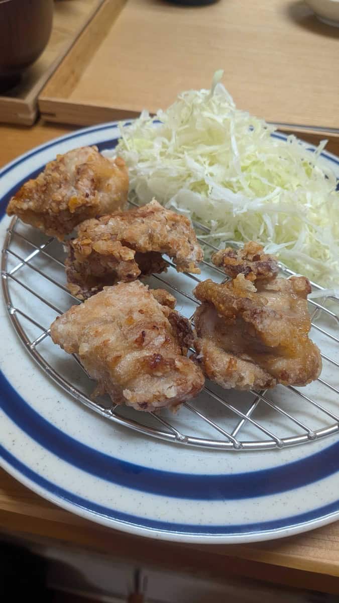 Four pieces of air fryer karaage on a round wire rack with shredded cabbage on a blue-striped plate