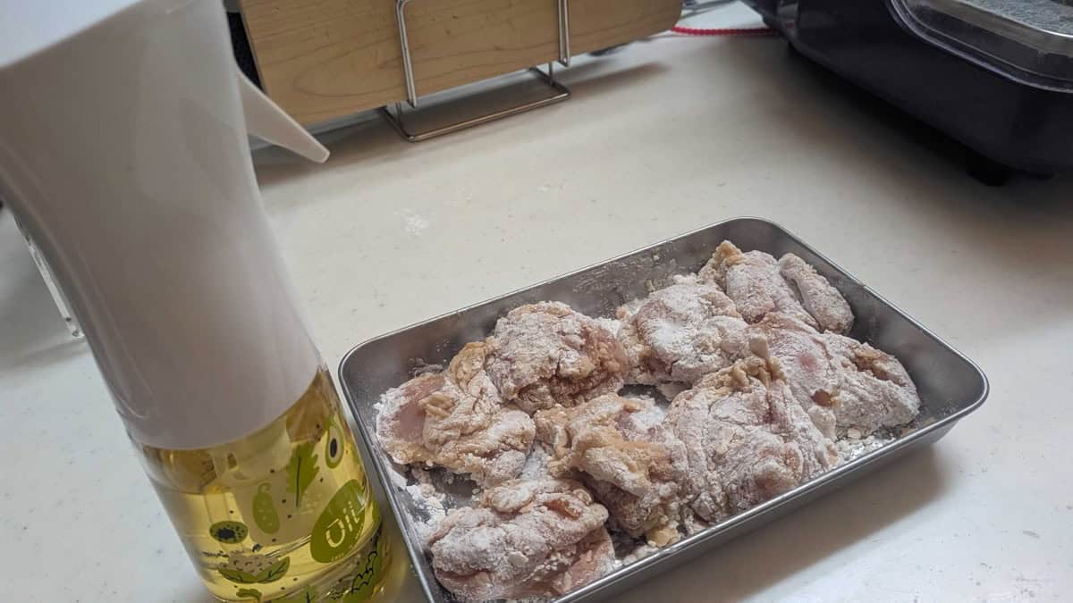 A refillable spray bottle of rice oil next to a tray of chicken coated in potato starch