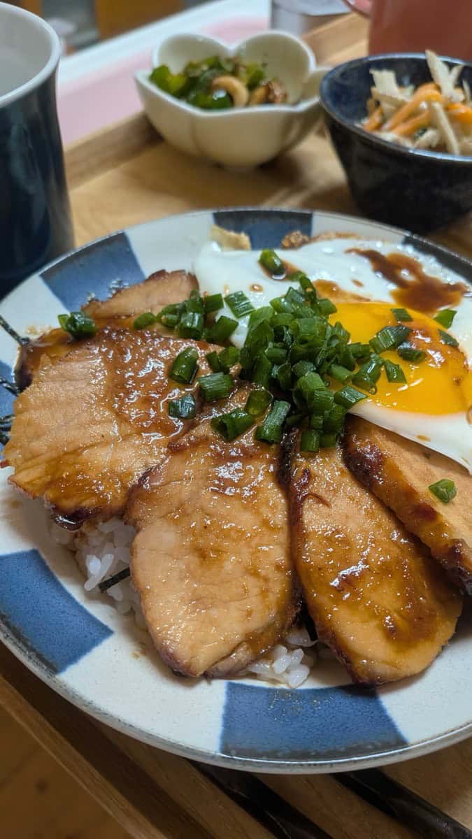 Chashu don — sliced Japanese pork loin chashu over rice with a fried egg and chopped green onion, on a blue and white plate