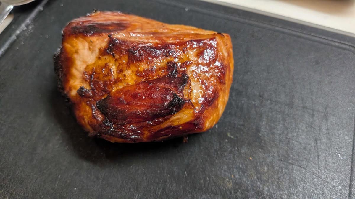 A whole block of air fryer chashu with a dark glazed crust resting on a black cutting board