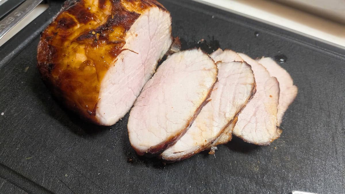 Air fryer pork loin chashu sliced thin on a cutting board, showing the pale pink juicy interior and dark glazed edge
