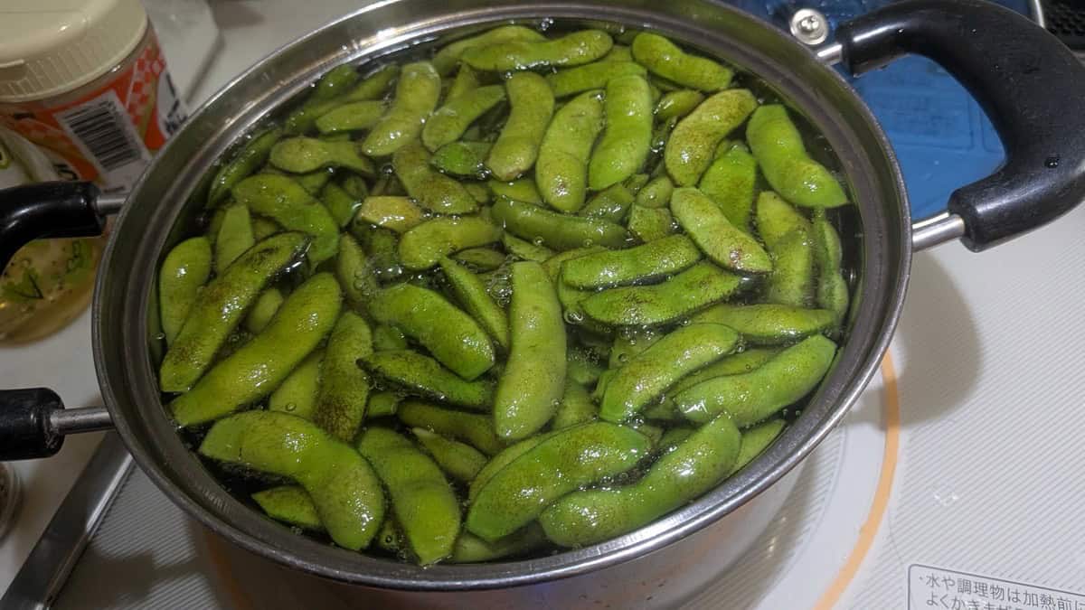 Edamame pods boiling in a pot of salted water, turned bright green