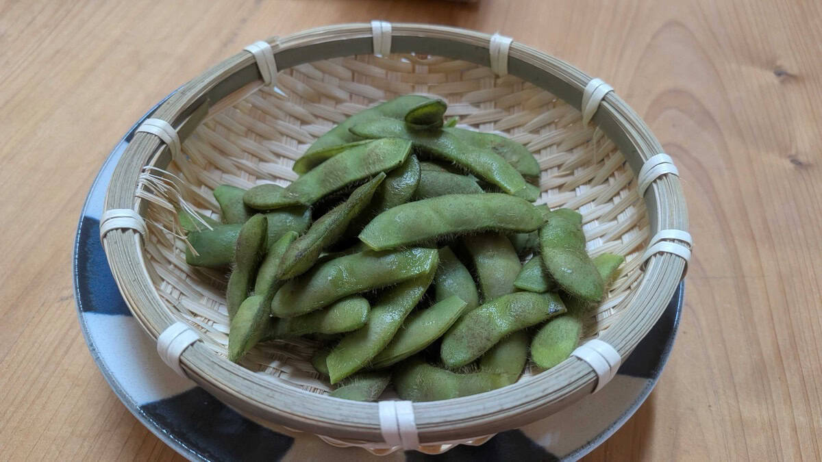 Finished boiled edamame served in a bamboo basket on a blue and white plate