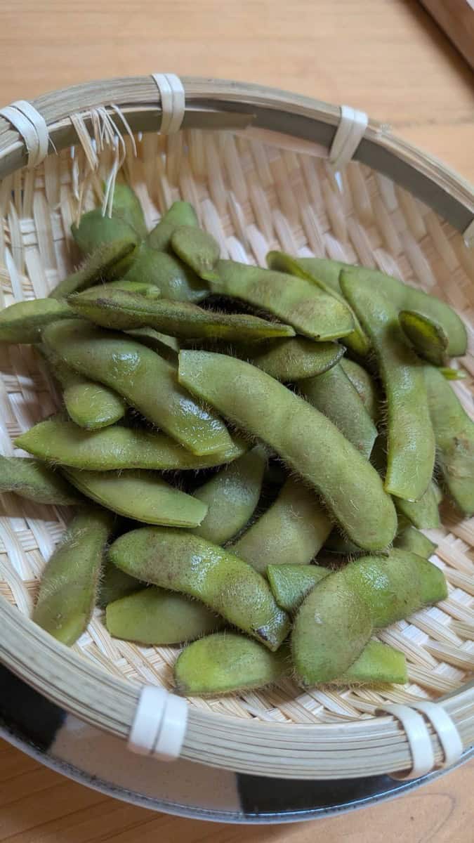 Boiled Japanese edamame in a bamboo basket, pods still bright green and lightly salted