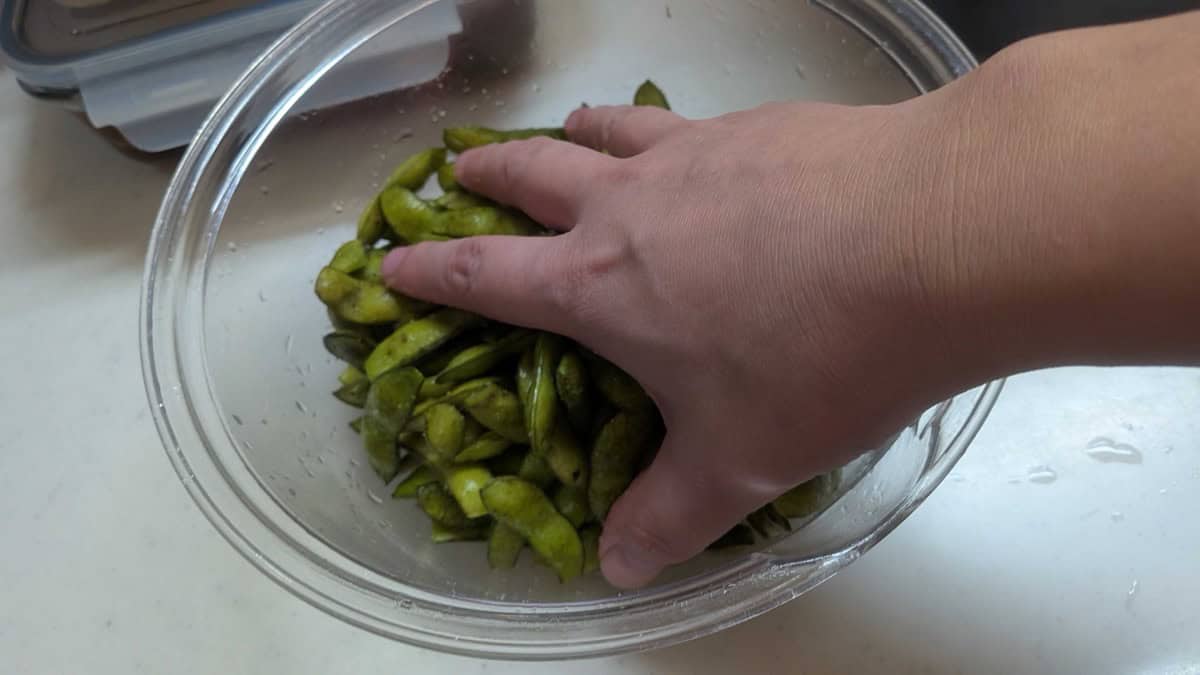 Rubbing salt into edamame pods by hand in a glass bowl to remove the fuzzy hairs