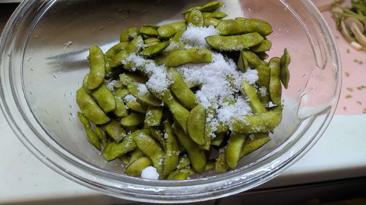 Edamame pods in a glass bowl with a tablespoon of salt scattered over them