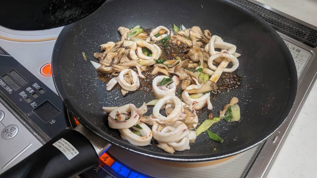 The soy sauce and mirin added to the pan, bubbling around the squid, mushrooms and spring onion