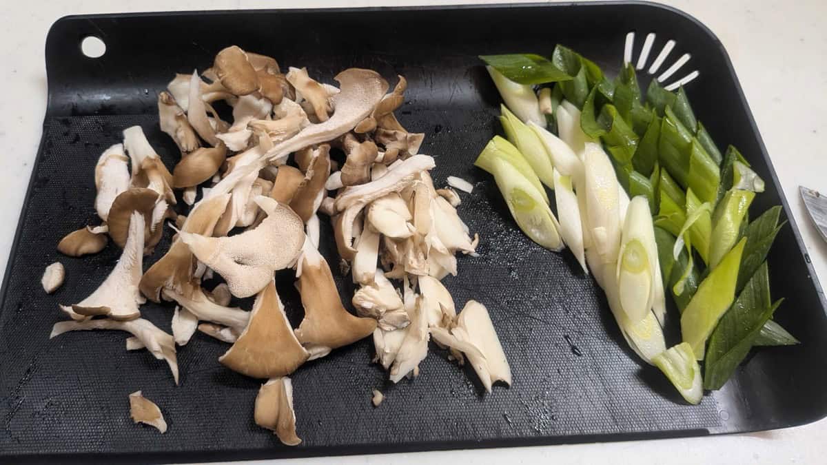 Torn maitake mushrooms and diagonally cut spring onion on a black cutting board