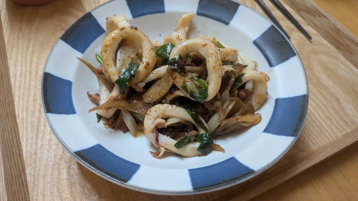 The finished squid butter stir-fry plated on a blue and white striped plate with chopsticks alongside