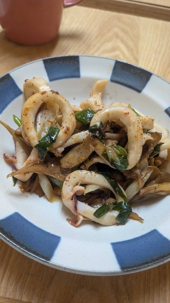 Japanese squid with butter and soy sauce — squid rings with maitake mushrooms and spring onion on a blue and white plate