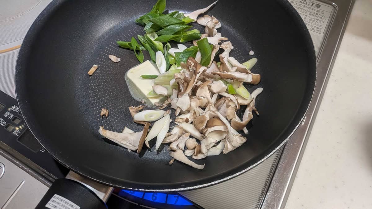 Spring onion, a pat of butter and torn maitake mushrooms in a frying pan on an IH cooktop