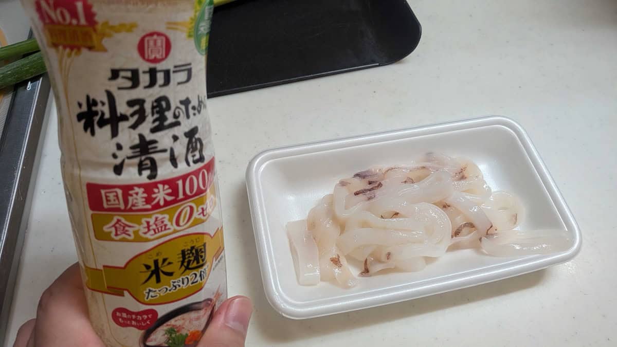 A bottle of Takara cooking sake held next to the tray of raw squid rings