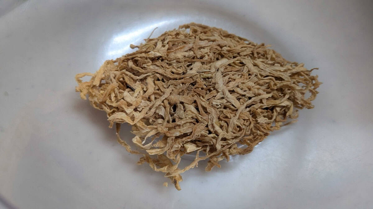 Dried shredded daikon radish strips on a white plate before soaking, pale tan and brittle