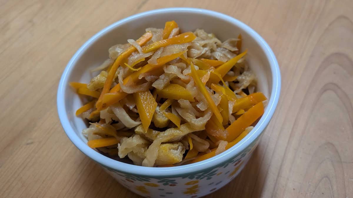 Kiriboshi daikon served in a white bowl on a wooden table, with strands of daikon, carrot and fried tofu glossy with broth