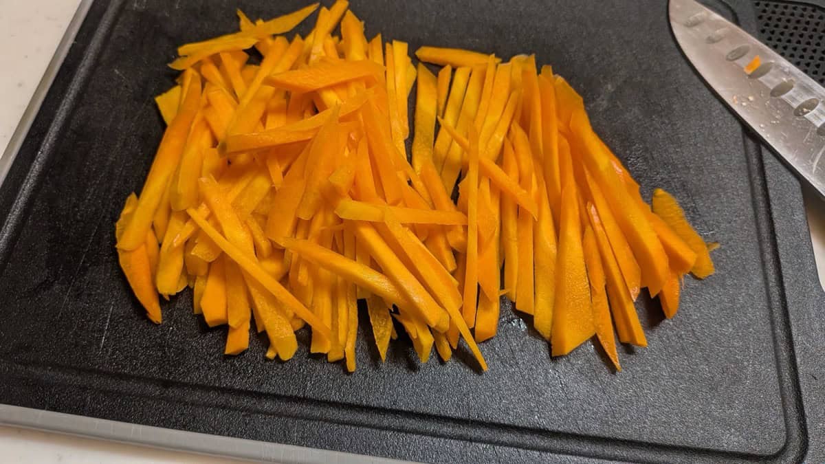Carrot cut into matchsticks on a black cutting board next to a knife